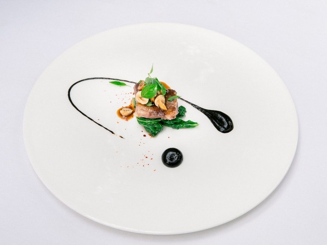 Fine-dining dish arranged with greens, meat, nuts, and black sauce