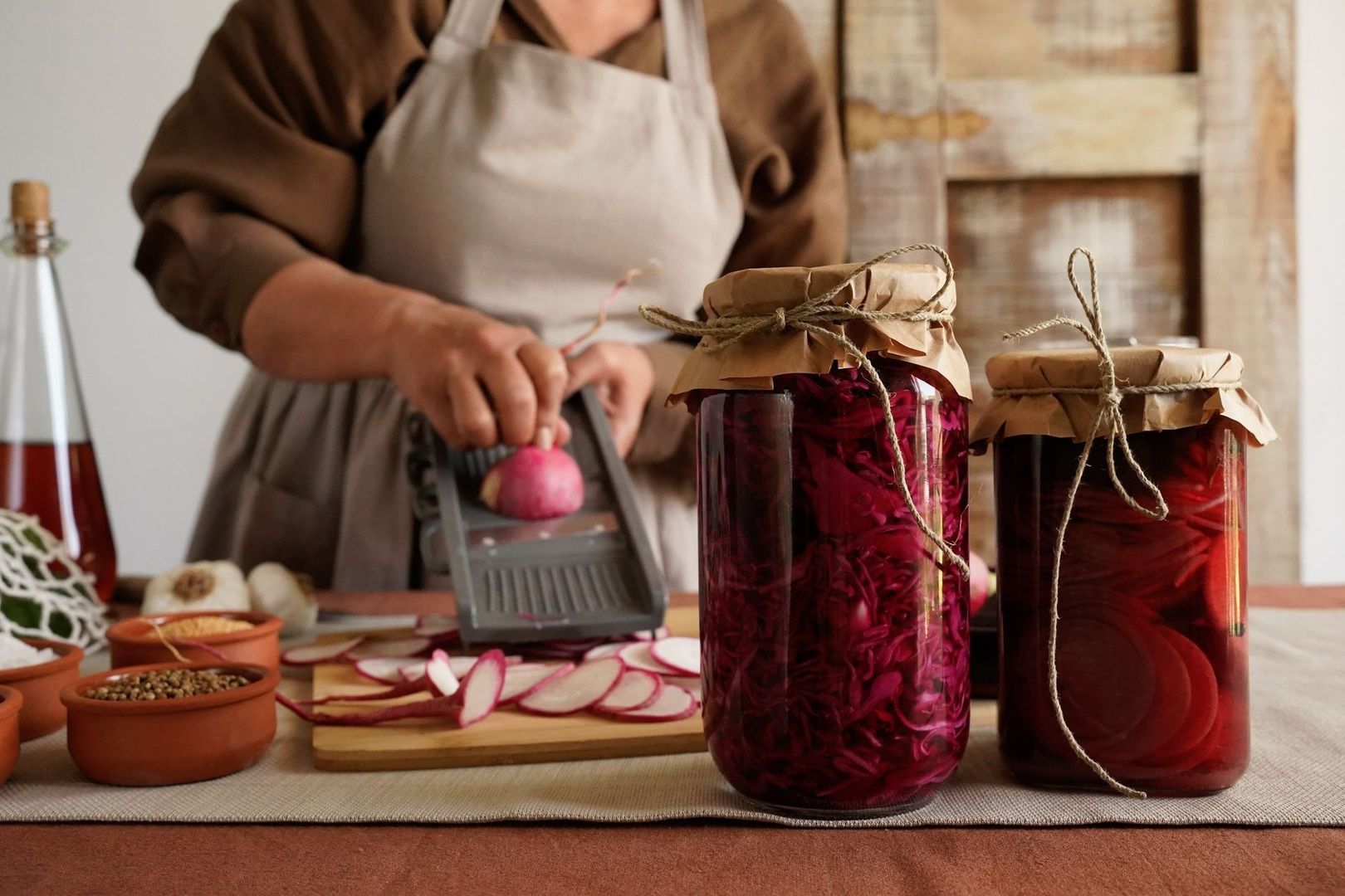 Person preparing radishes beside jars of preserved vegetables